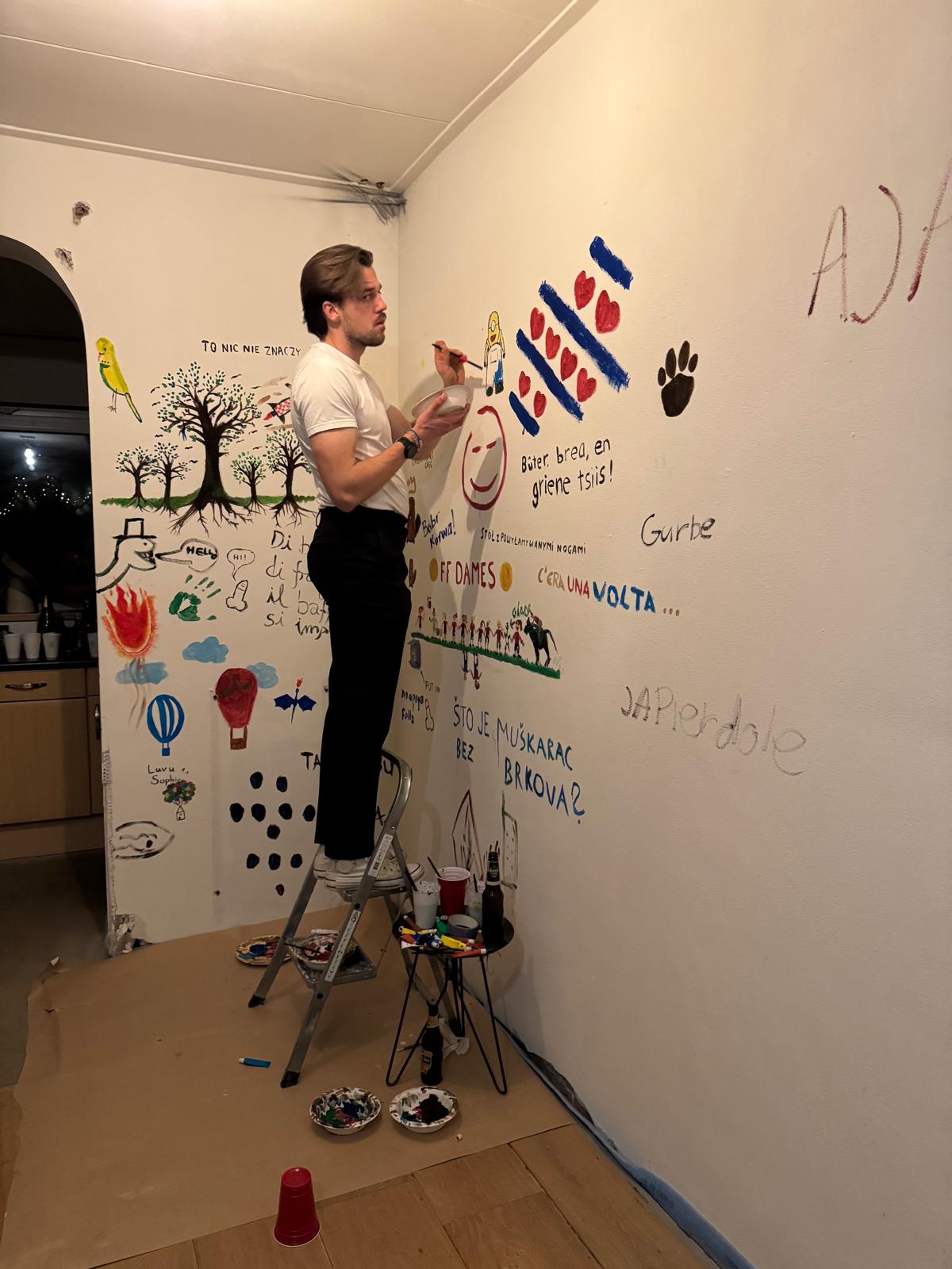 Greg painting a mural on the wall, surrounded by other guests' artwork